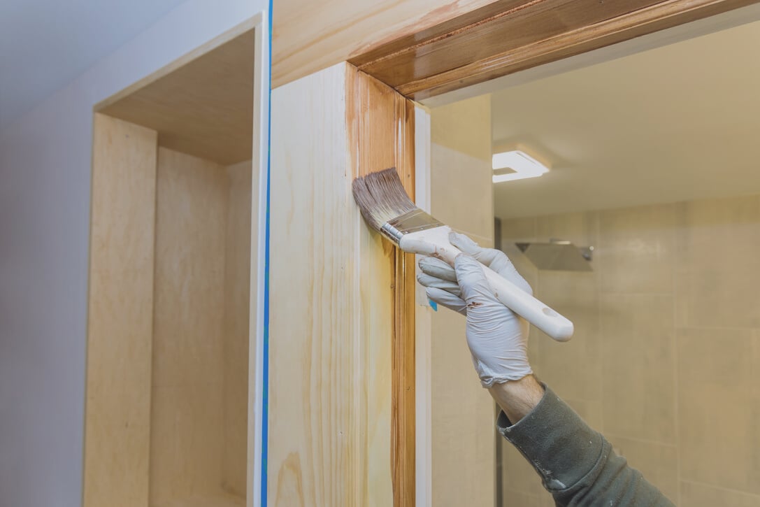 Hand of Repairman Painting with Gloves in the a Brush Applying Varnish Paint Wood Doors Molding Trim with Paintbrush